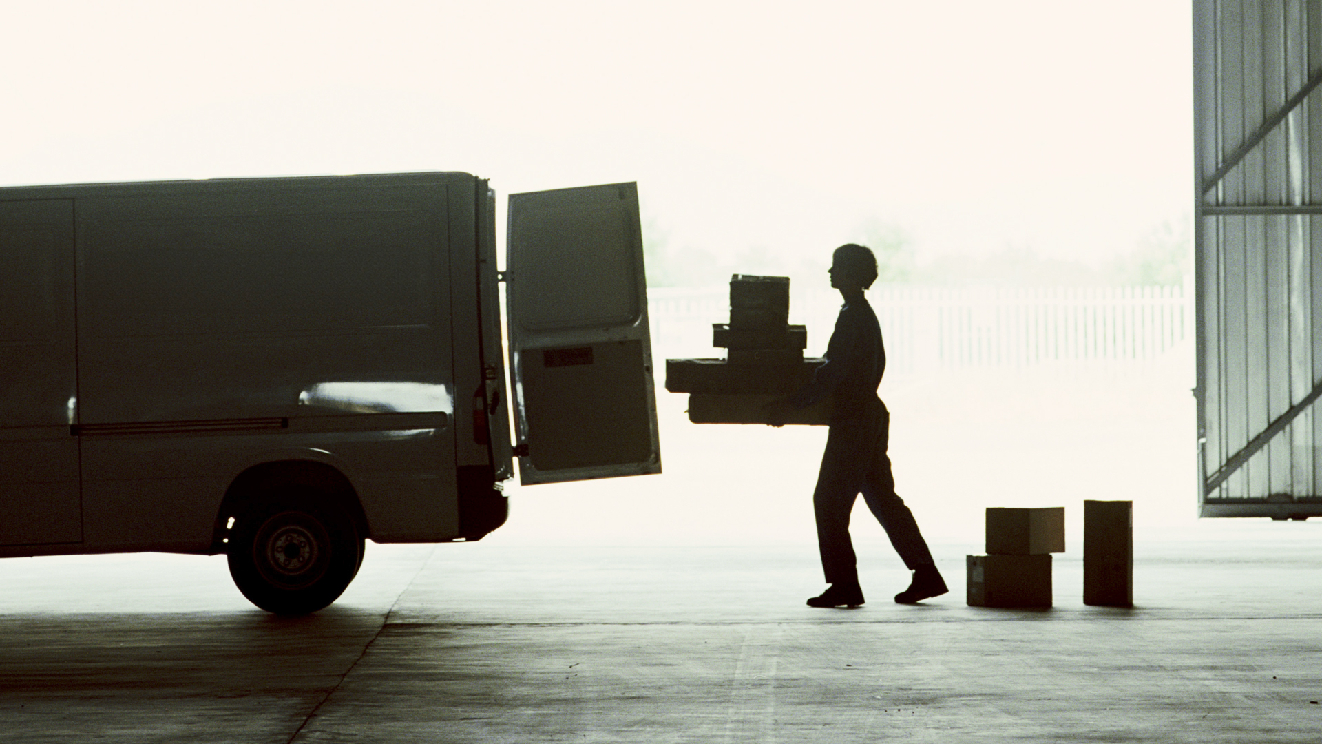 Silhouette of a delivery worker loading parcels into a cargo van in a warehouse, highlighting seamless first-mile logistics and streamlined pick-up operations.